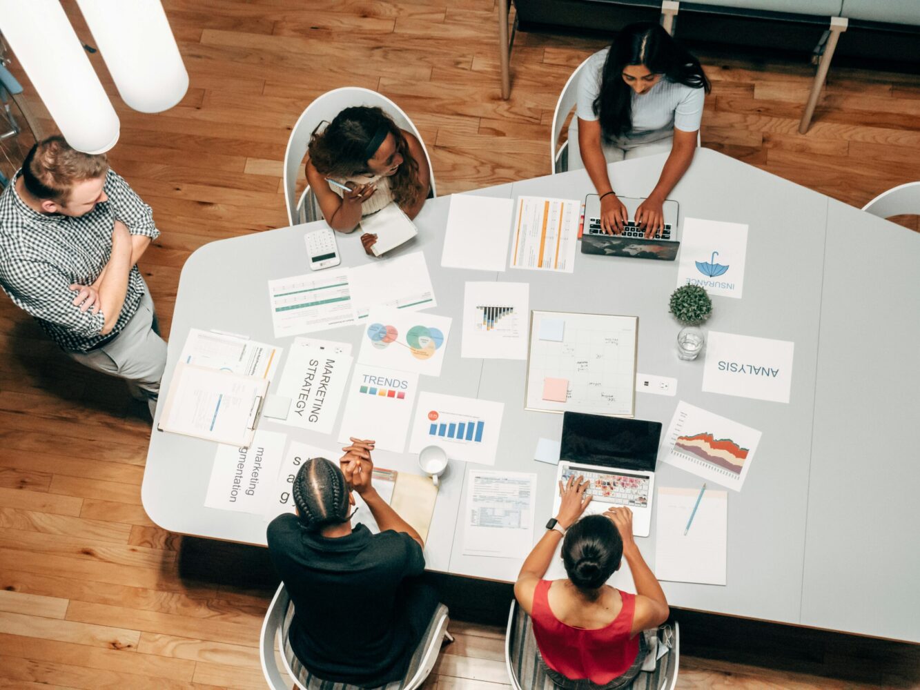 4 people having a marketing meeting sitting around a table, with many pieces of paper with charts on them